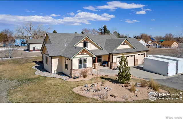 view of front of house with an attached garage, fence, stone siding, driveway, and roof with shingles