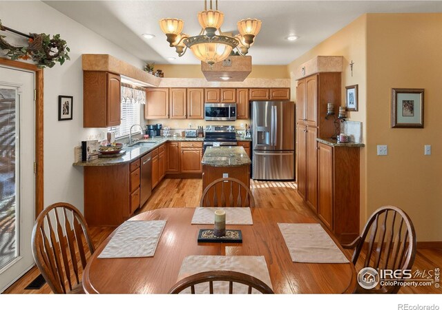 kitchen featuring a sink, appliances with stainless steel finishes, a center island, light wood finished floors, and an inviting chandelier