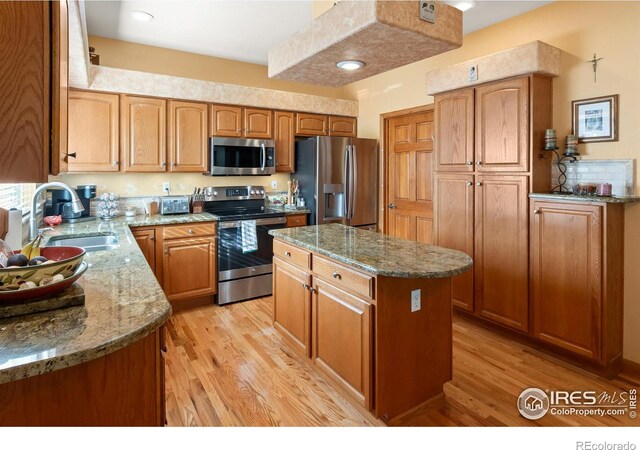 kitchen with stainless steel appliances, a kitchen island, a sink, and light stone countertops