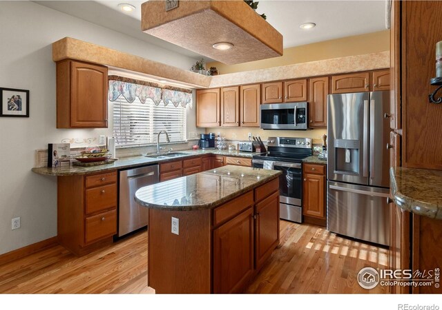 kitchen with a sink, light wood-style floors, appliances with stainless steel finishes, a center island, and brown cabinetry