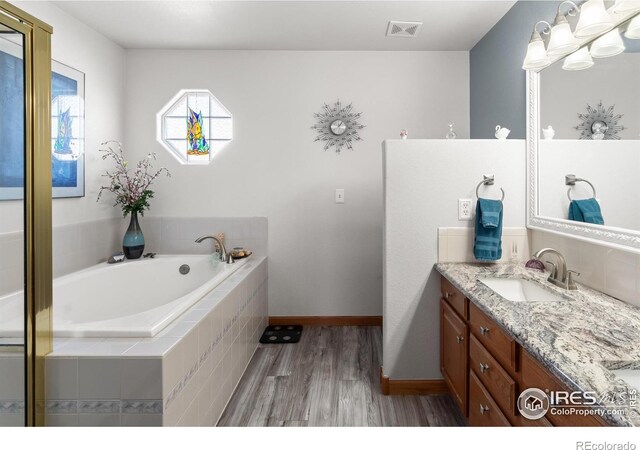 bathroom with baseboards, visible vents, wood finished floors, a garden tub, and vanity