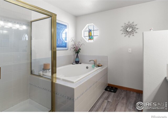 bathroom featuring a garden tub, baseboards, wood finished floors, and a shower stall