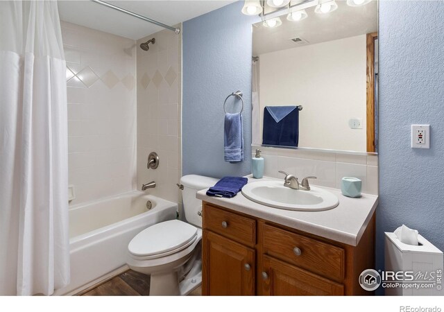 full bath featuring shower / tub combo with curtain, a textured wall, vanity, and toilet