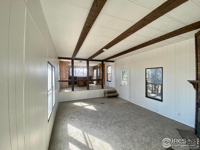 unfurnished living room with carpet floors, beam ceiling, and plenty of natural light