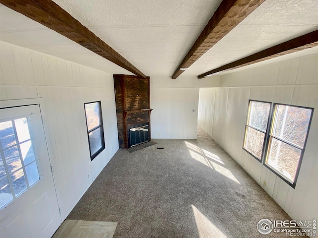 unfurnished living room with a brick fireplace, carpet, plenty of natural light, and beam ceiling