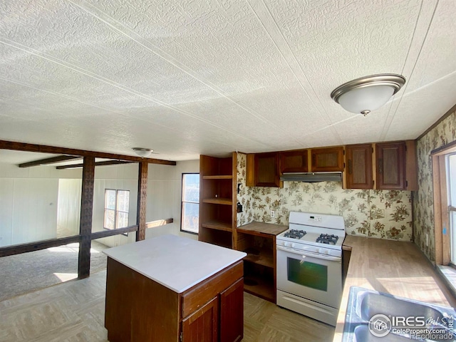 kitchen featuring wallpapered walls, white range with gas cooktop, a center island, light countertops, and under cabinet range hood