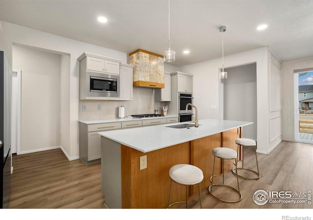 kitchen with light countertops, backsplash, appliances with stainless steel finishes, a sink, and light wood-type flooring