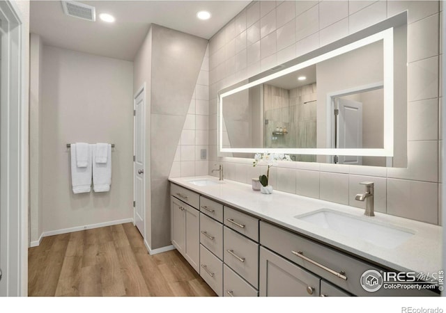 full bathroom with tasteful backsplash, visible vents, a tile shower, and a sink