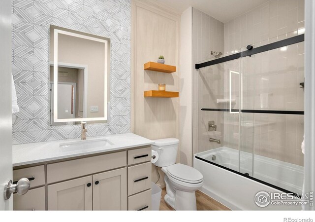 bathroom featuring toilet, shower / bath combination with glass door, vanity, and wallpapered walls