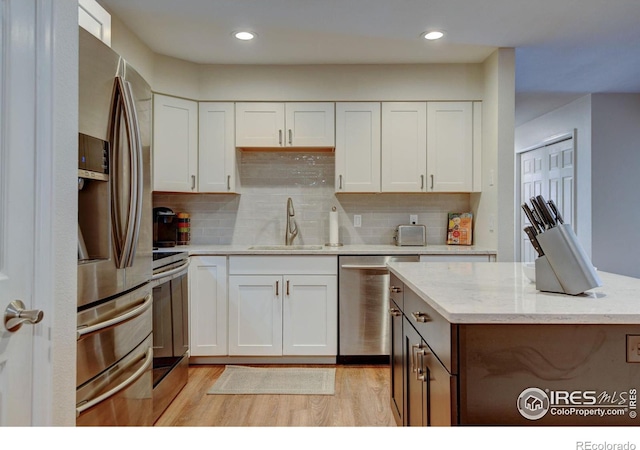 kitchen with appliances with stainless steel finishes, a sink, light wood-style flooring, and white cabinets