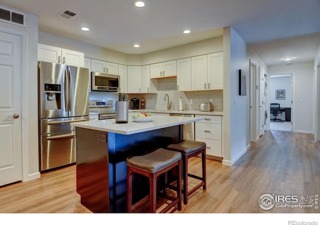 kitchen with a kitchen island, visible vents, light wood-style floors, appliances with stainless steel finishes, and a kitchen bar