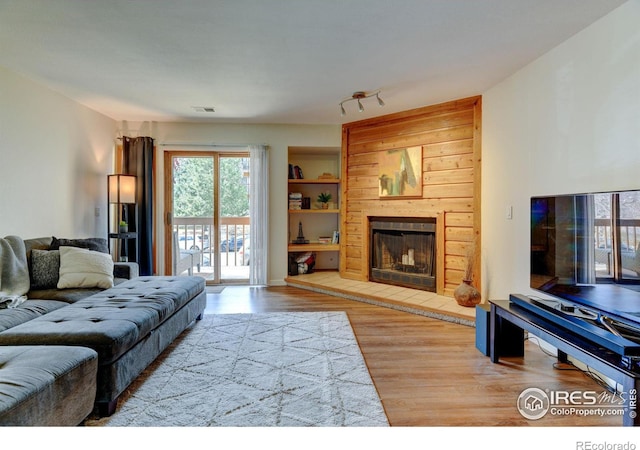 living room featuring a large fireplace, built in shelves, wood finished floors, and visible vents