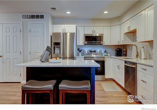 kitchen featuring a breakfast bar area, stainless steel appliances, a sink, visible vents, and light wood-style floors