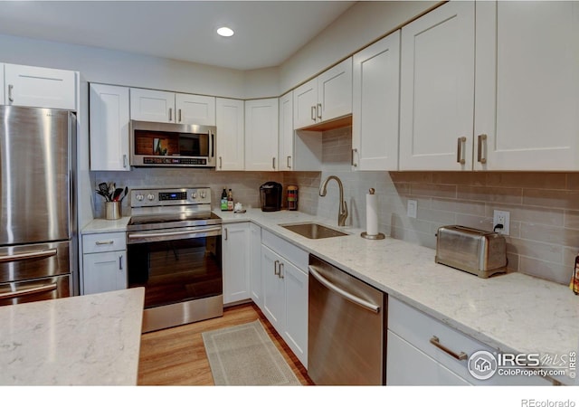 kitchen with stainless steel appliances, light wood-style flooring, decorative backsplash, white cabinets, and a sink