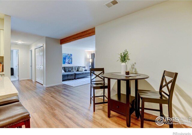 dining space with light wood-style flooring, beamed ceiling, visible vents, and baseboards