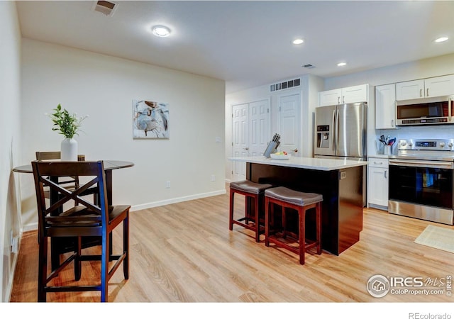 kitchen featuring light wood-style flooring, a breakfast bar, a kitchen island, white cabinetry, and appliances with stainless steel finishes