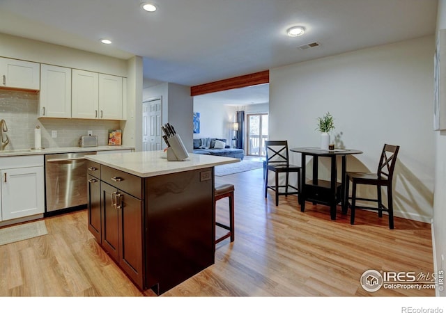 kitchen featuring a center island, visible vents, stainless steel dishwasher, light wood-style floors, and a kitchen breakfast bar