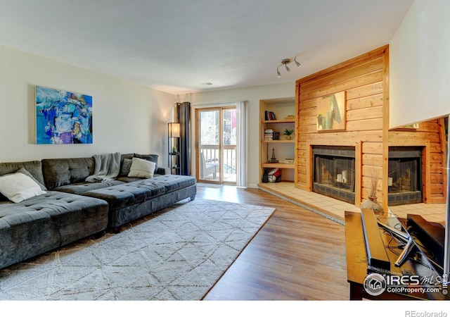 living room with built in shelves, a fireplace, and wood finished floors