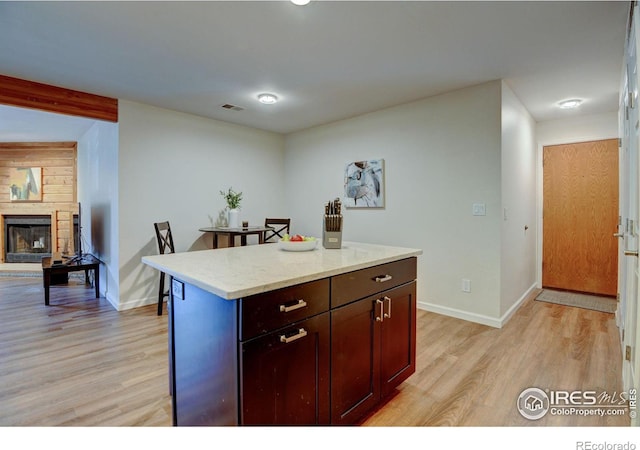 kitchen featuring baseboards, a fireplace, and light wood finished floors