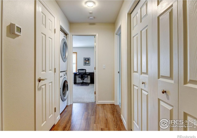 washroom with wood finished floors, stacked washer and clothes dryer, baseboards, and laundry area