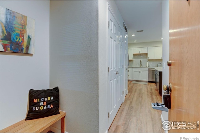 hall with light wood finished floors, a sink, visible vents, and recessed lighting