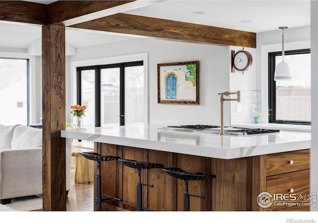 kitchen featuring light stone counters, hanging light fixtures, open floor plan, beamed ceiling, and a kitchen breakfast bar