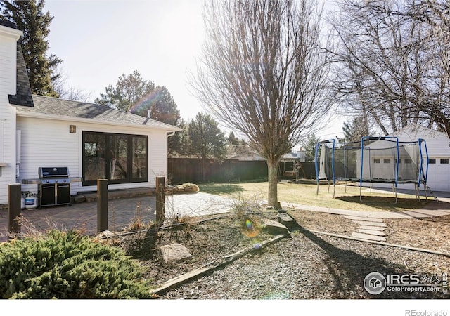 view of yard featuring a trampoline, a patio area, and fence