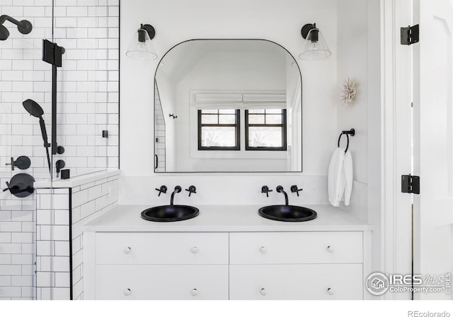 bathroom featuring double vanity, tiled shower, and a sink