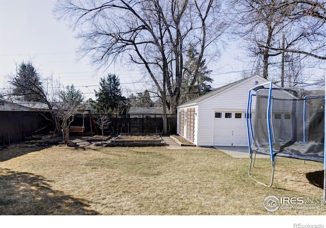 view of yard featuring a trampoline, a fenced backyard, an outdoor structure, and a garage