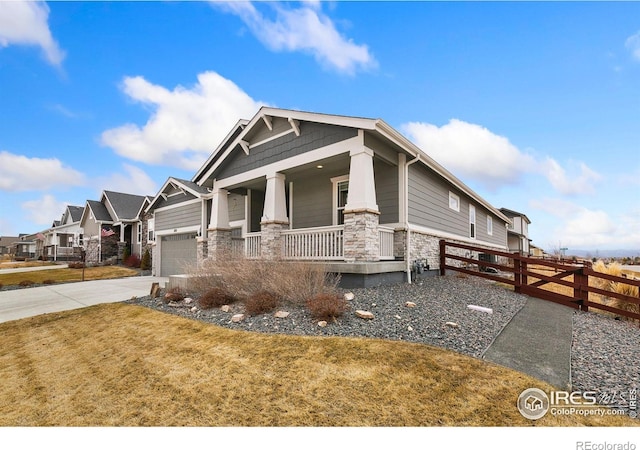 craftsman-style home with covered porch, fence, a garage, stone siding, and driveway