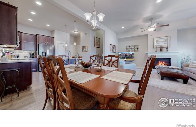 dining space featuring ceiling fan with notable chandelier, recessed lighting, a glass covered fireplace, and light wood-style floors