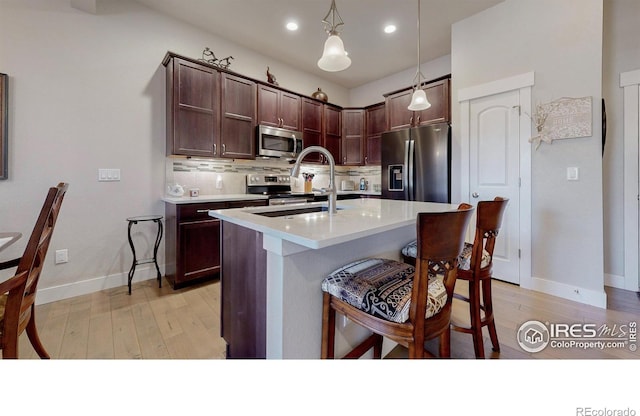 kitchen featuring a breakfast bar, light wood finished floors, tasteful backsplash, light countertops, and appliances with stainless steel finishes