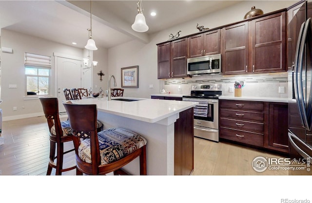 kitchen with tasteful backsplash, appliances with stainless steel finishes, a kitchen breakfast bar, light countertops, and a sink