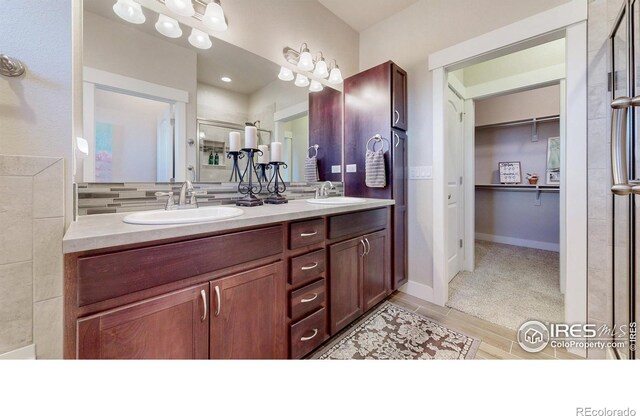 full bath featuring a walk in closet, a sink, baseboards, and double vanity