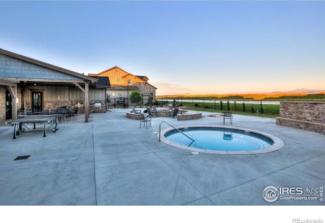 pool at dusk featuring a fire pit, a patio area, fence, and a hot tub