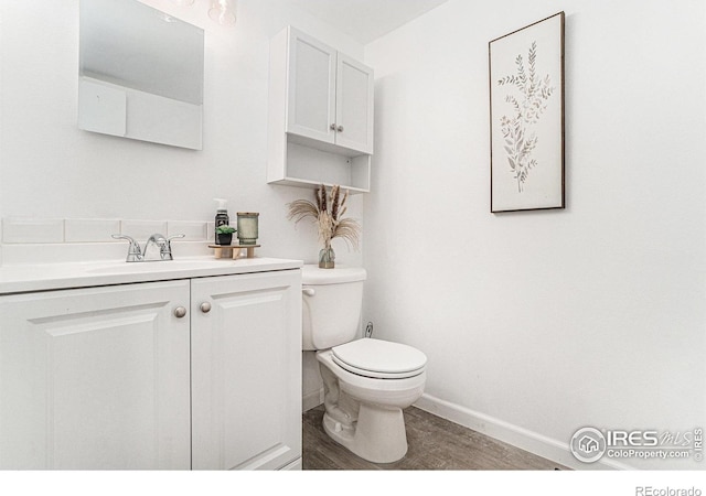 half bath with wood finished floors, vanity, toilet, and baseboards