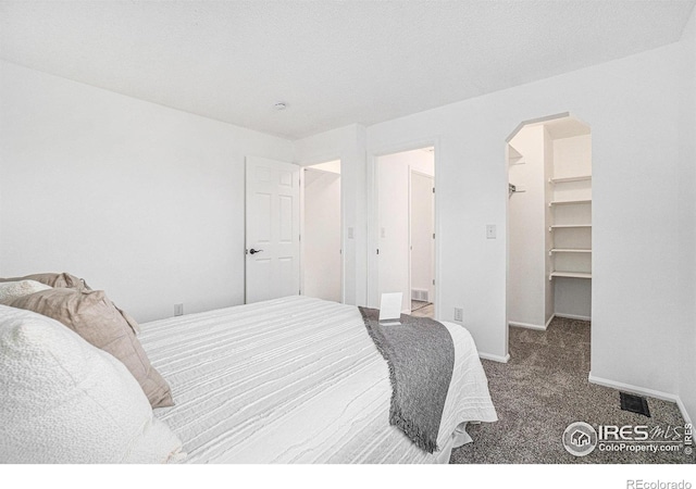 bedroom featuring carpet floors, a walk in closet, arched walkways, visible vents, and baseboards