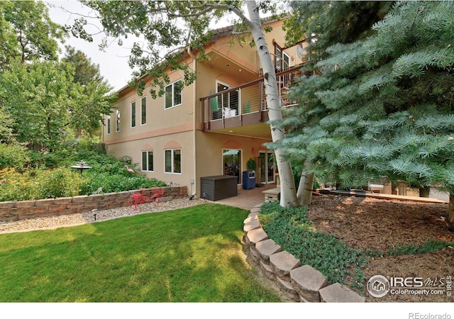 back of house featuring a patio, a lawn, a balcony, and stucco siding