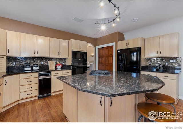 kitchen featuring arched walkways, a breakfast bar area, wood finished floors, light brown cabinetry, and black appliances