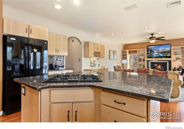 kitchen with a warm lit fireplace, black fridge with ice dispenser, visible vents, gas stovetop, and light brown cabinetry