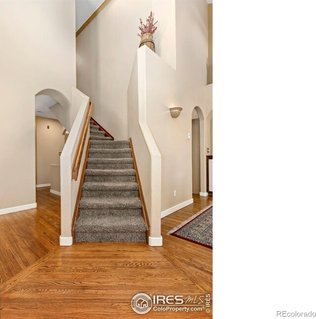 staircase featuring a towering ceiling, arched walkways, and wood finished floors