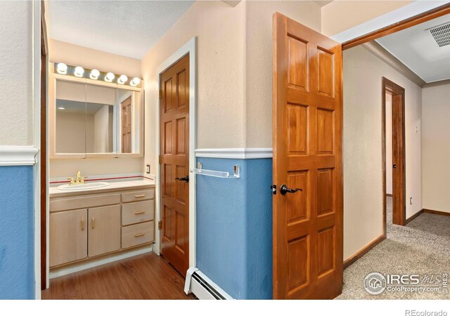 bathroom with visible vents, a baseboard heating unit, vanity, wood finished floors, and baseboards