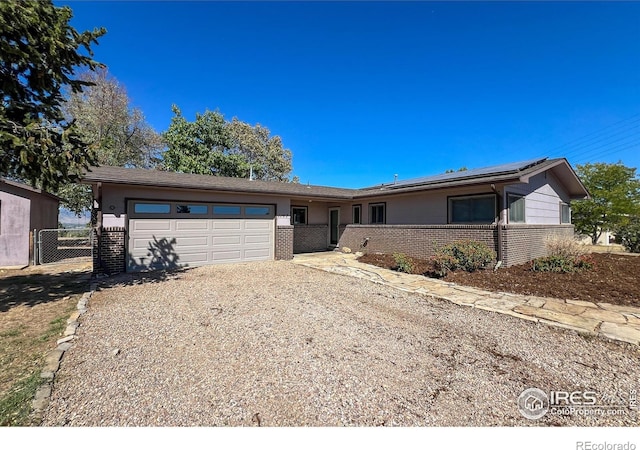 ranch-style house with a garage, solar panels, brick siding, driveway, and a gate