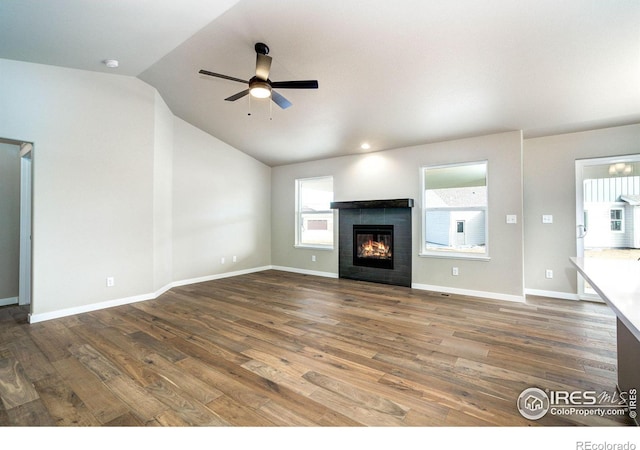 unfurnished living room featuring lofted ceiling, ceiling fan, wood finished floors, baseboards, and a glass covered fireplace