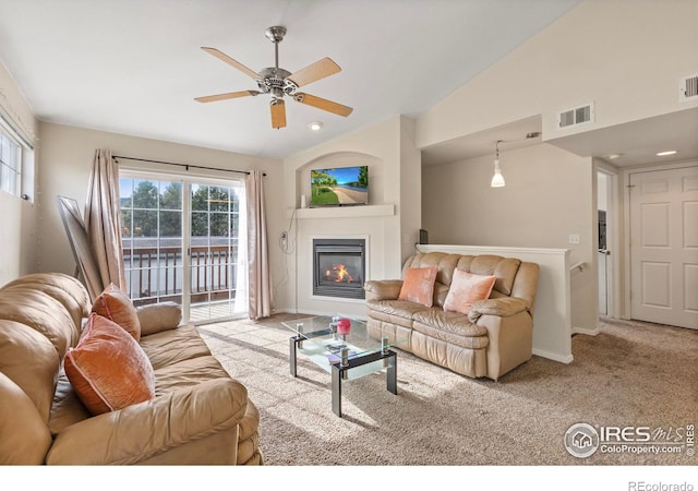 carpeted living room featuring ceiling fan, visible vents, vaulted ceiling, and a glass covered fireplace