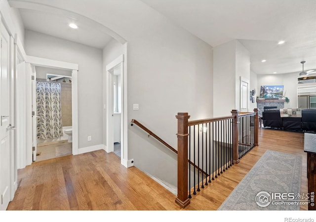 hall with arched walkways, recessed lighting, an upstairs landing, wood finished floors, and baseboards