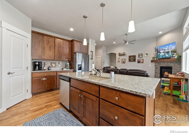 kitchen featuring appliances with stainless steel finishes, decorative light fixtures, a stone fireplace, light wood-type flooring, and a sink