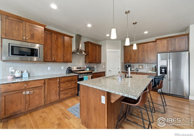 kitchen featuring light wood finished floors, wall chimney exhaust hood, stainless steel appliances, and a sink