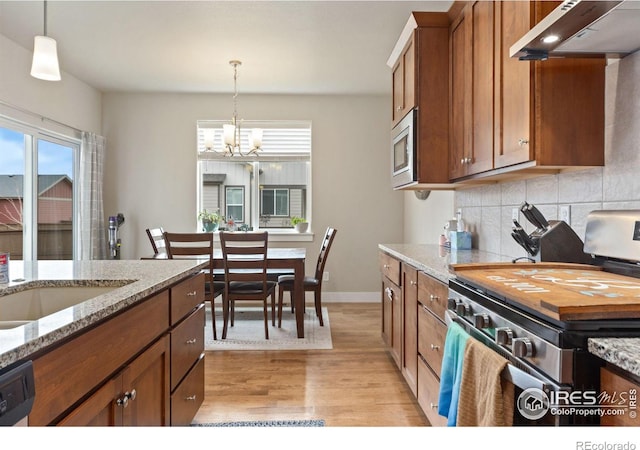 kitchen featuring tasteful backsplash, brown cabinets, hanging light fixtures, stainless steel appliances, and under cabinet range hood