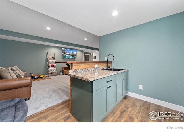 kitchen with open floor plan, wood finished floors, a peninsula, light countertops, and a sink